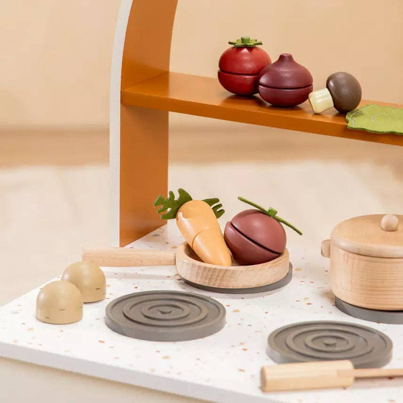 Wooden toy kitchen set with pots, pans, and vegetables on a beige shelf.