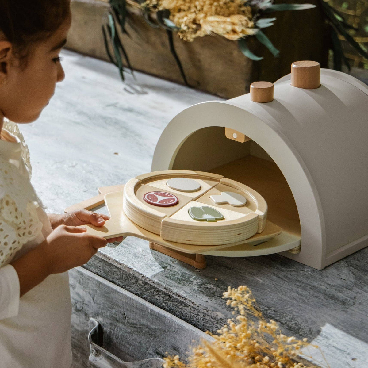 Child with a toy pizza oven and play food on a wooden surface