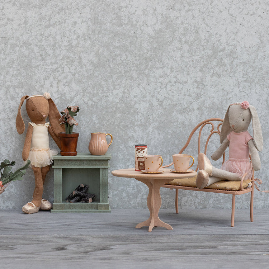 Miniature dollhouse scene with rabbits and furniture against a textured wall.