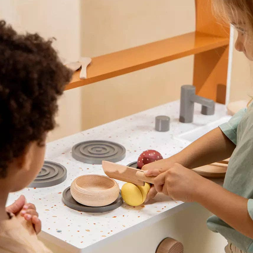 Two children playing with a wooden toy kitchen set 